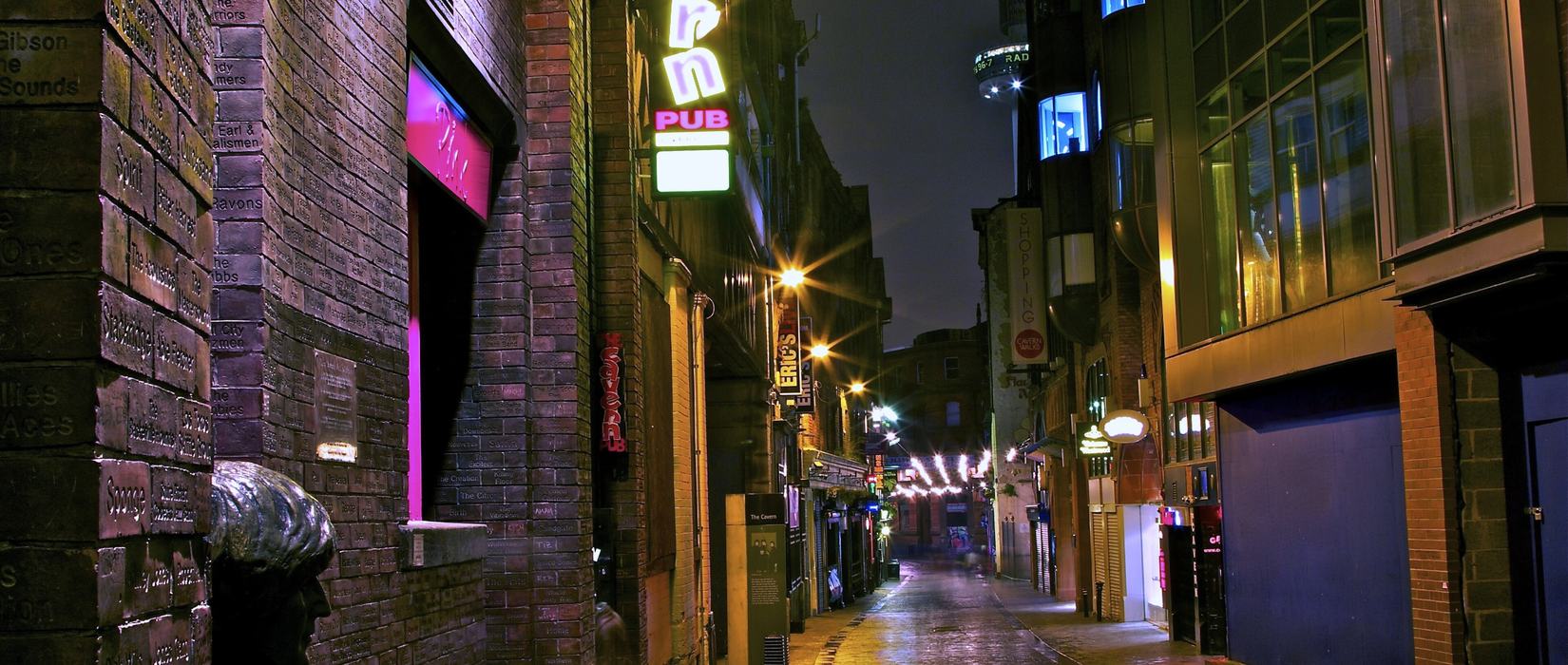 A quiet city street at night, shopfronts still glowing along an empty footpath